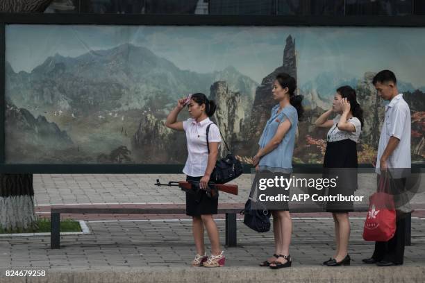 In a photo taken on July 29 a woman holds a mock rifle as she stands with others at a trolley bus stop in Pyongyang. Buses and trams are by far the...