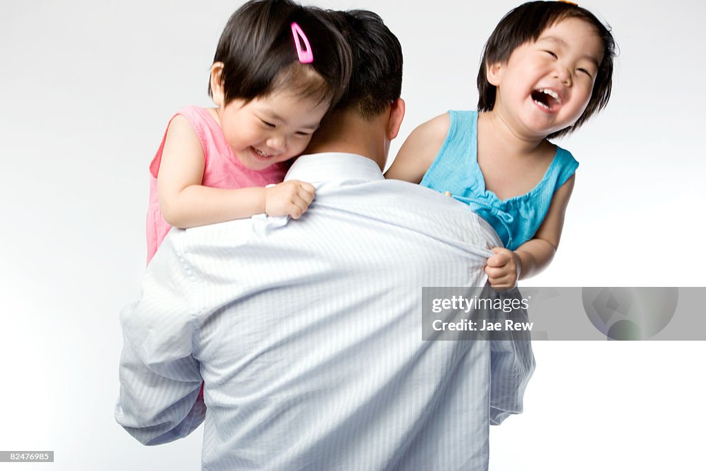 Twin kids peering over fathers arm and laughing