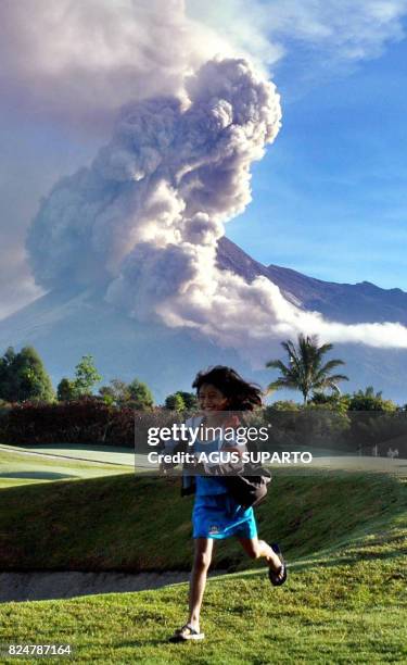 This photo taken on June 18, 2006 shows Indonesian girls playing at a golf course in Sleman, near Yogyakarta, as a cloud of ash rises from Mount...
