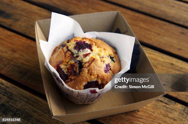 mixed berry, white chocolate and coconut muffin in waxed paper in a cardboard tray on a wooden outdoor table - muffins stock pictures, royalty-free photos & images