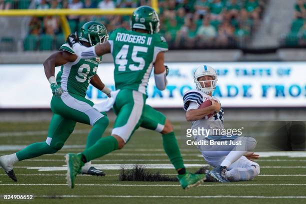 Ricky Ray of the Toronto Argonauts slides after scrambling to avoid a hit from Tobi Antigha and Kacy Rodgers II of the Saskatchewan Roughriders in...