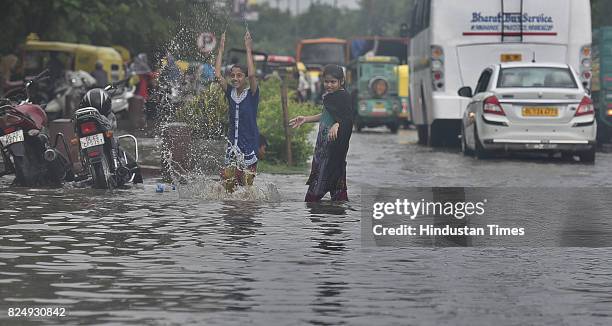 Children enjoy rain water as vehicles wade through logged rain water during a heavy rainfall at Delhi Gate on July 31, 2017 in New Delhi, India....