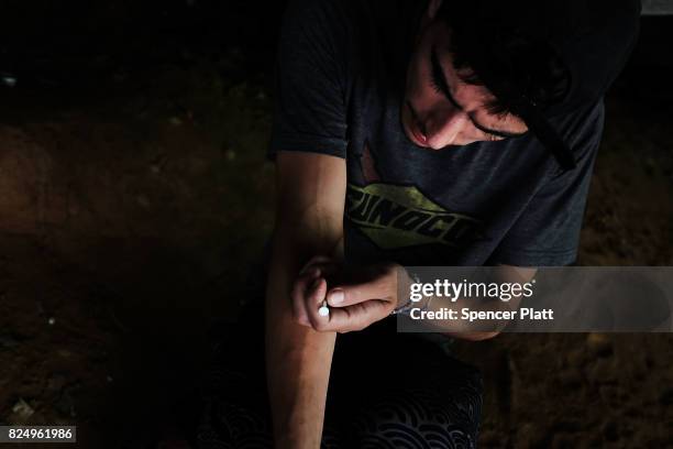 Mike a heroin addict who began using opiates when he was 13, pauses to shoot-up by a railway underpass in the Kensington section of Philadelphia...