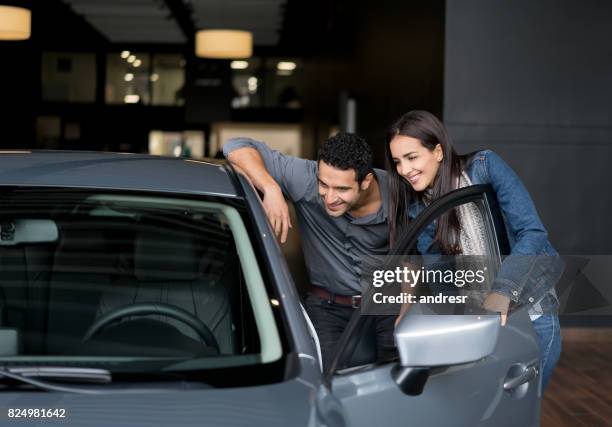 couple looking at a car to buy at the dealership - new imagens e fotografias de stock