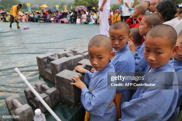 This photo taken on July 30, 2017 shows young Shaolin monks looking on beside stone locks during the first "72 Arts of Shaolin" martial arts...