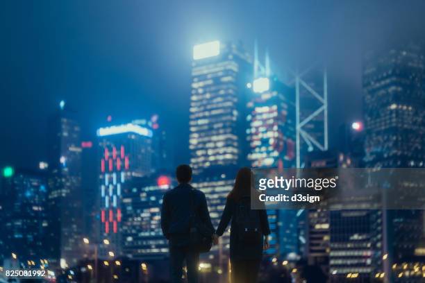 couple holding hands against illuminated urban cityscape at night - asien metropole nachtleben stock-fotos und bilder