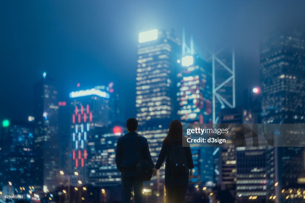 Couple holding hands against illuminated urban cityscape at night