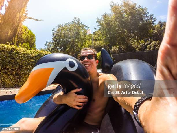 happy guy taking a selfie enjoying summer in swimming pool with big inflatable black swan sunbathing and relaxing in the sun during weekend. - gopro stock-fotos und bilder