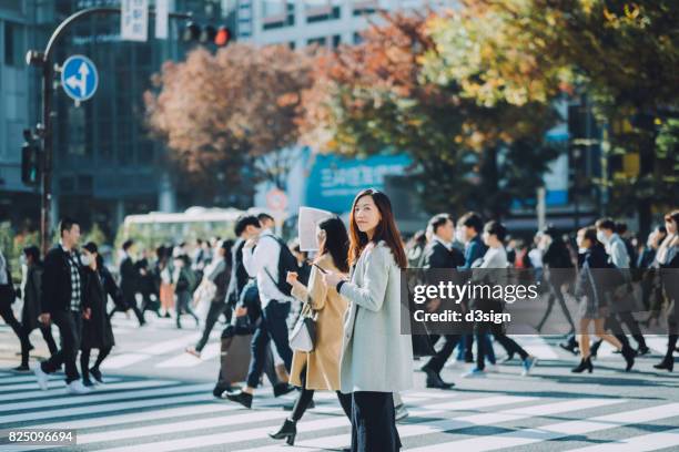 beautiful asian businesswoman using smartphone while walking on busy street in tokyo - bezirk shibuya stock-fotos und bilder