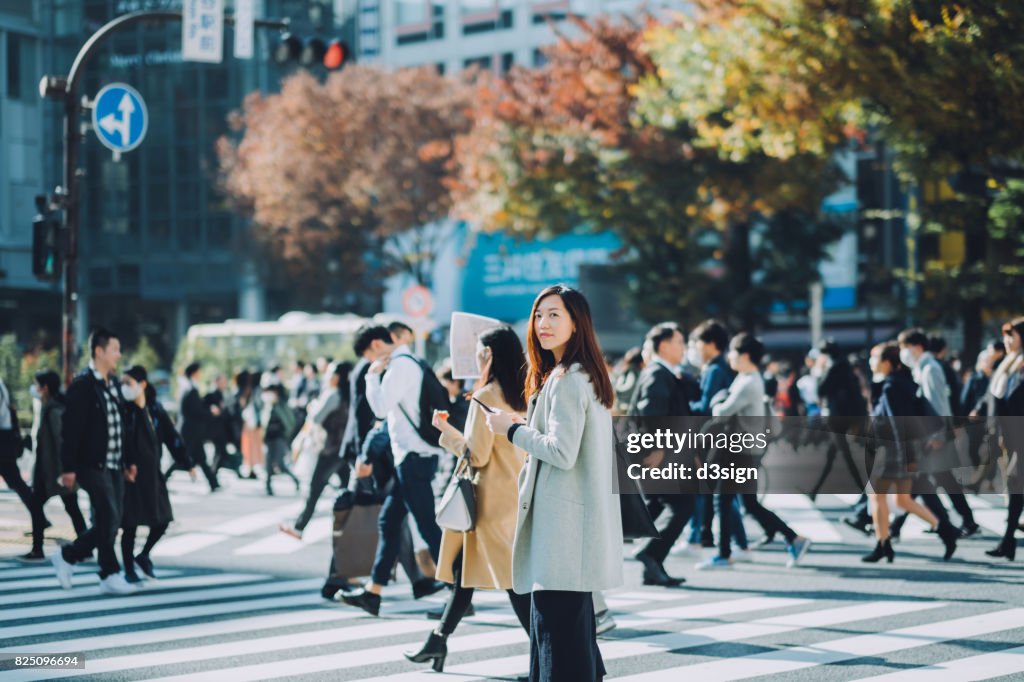 Beautiful Asian businesswoman using smartphone while walking on busy street in Tokyo