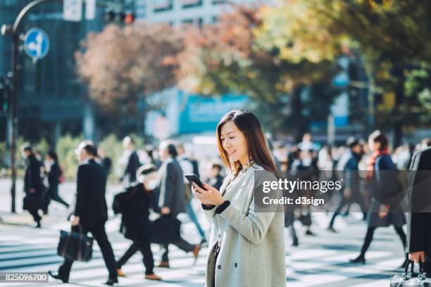 young smiling lady using smartphone outdoors in busy downtown city street - busy lifestyle stockfoto's en -beelden