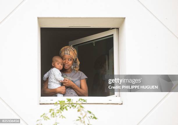 Sudanese migrant holding her baby poses at the window of a former hotel transformed into a shelter for Calais migrants on August 1, 2017 in Bailleul,...