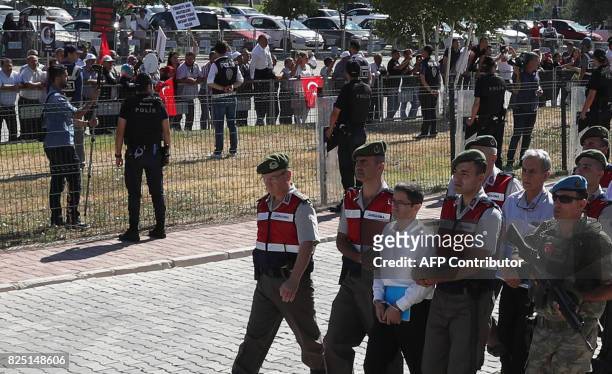 Defendants Kemal Batmaz and Akin Ozturk and other defendants are accompanied by gendarmerie as people protest as they arrive for their trial at...