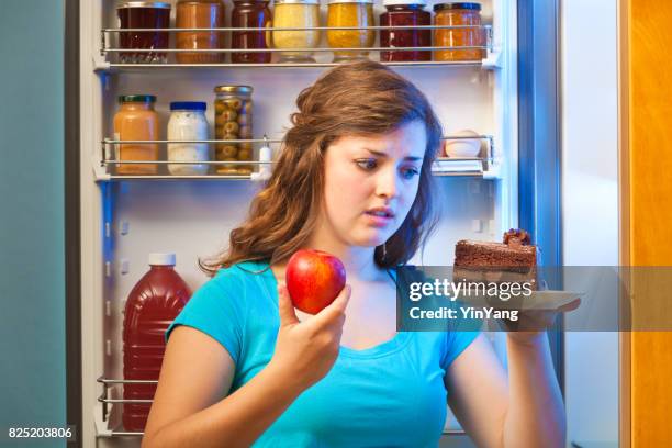 young woman making decision on healthy eating in front of refrigerator - caught in the act stock pictures, royalty-free photos & images