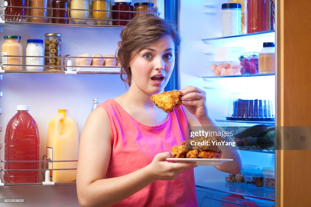 Junge Frau ungesund essen vor Kühlschrank
