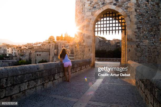 traveler woman contemplating the city from the old bridge of besalu town during travel vacations in the catalonia region with nice sunset warm light. - besalu stock pictures, royalty-free photos & images