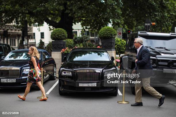 Two people walk past a row of cars including a Brabus and two Rolls Rocyes parked outside The Dorchester hotel in Mayfair on August 1, 2017 in...