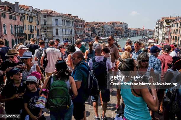 Large crowd of tourists stand on Rialto bridge on August 1, 2017 in Venice, Italy. Over 30 million tourists visit the 3 mile by 2 mile city of Venice...