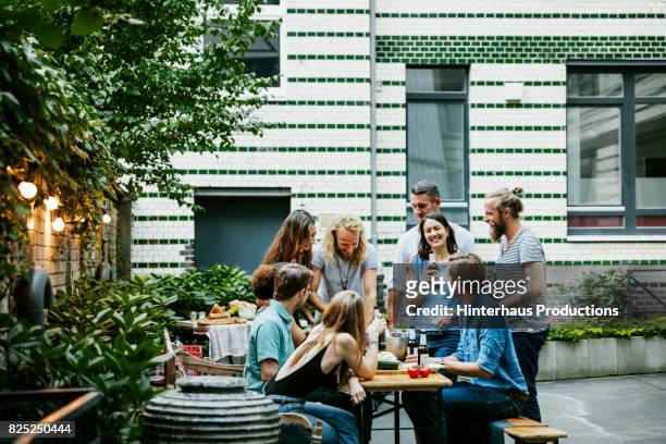 young group of friends gathered around table outside preparing for barbecue - barbecue social gathering stock pictures, royalty-free photos & images