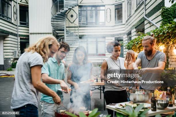 group of friends gathered at barbecue eating and socialising - kochen freunde stock-fotos und bilder