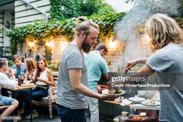 young man serving his friend food from barbecue - evening indulgence stock pictures, royalty-free photos & images