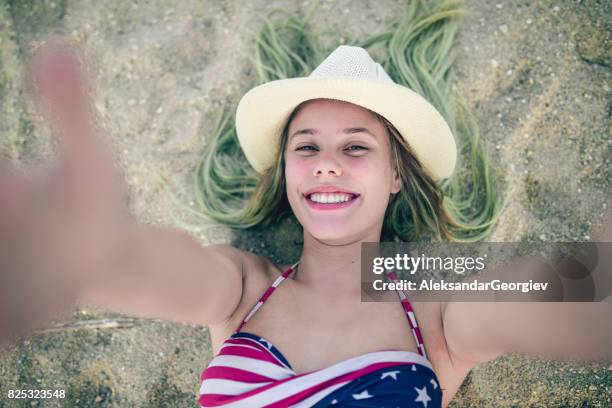 smiling girl with straw how lying on beach sand and taking selfie - girl and blond hair and cowboy hat stock pictures, royalty-free photos & images