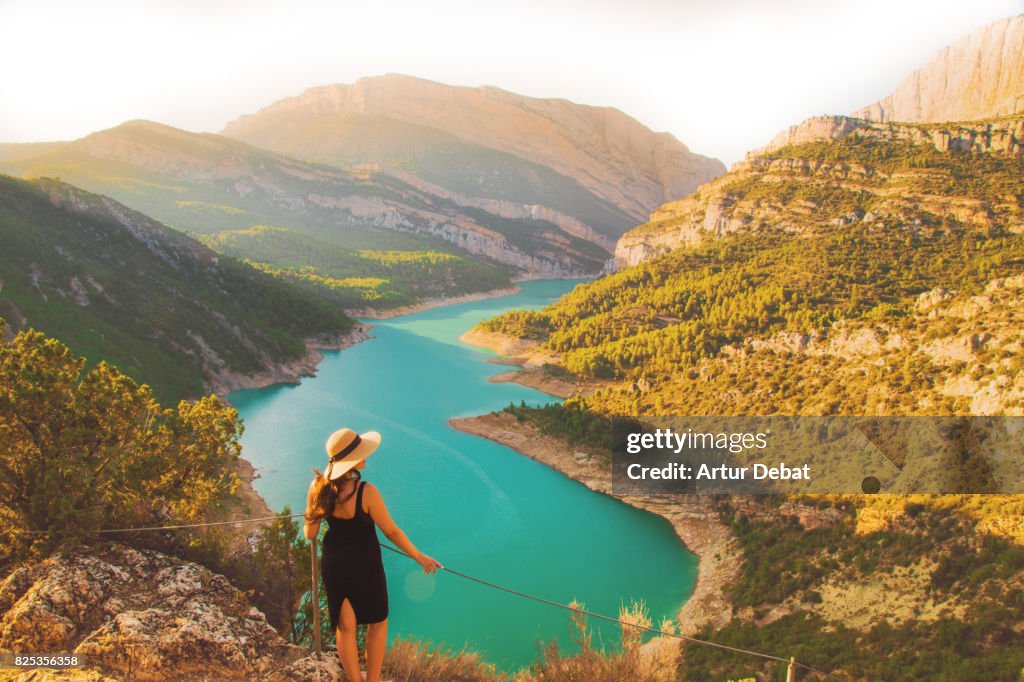 Traveler woman contemplating the stunning view from viewpoint on top of the edge with cliff and stunning views of the lake and mountains in the Catalan Pyrenees mountains.