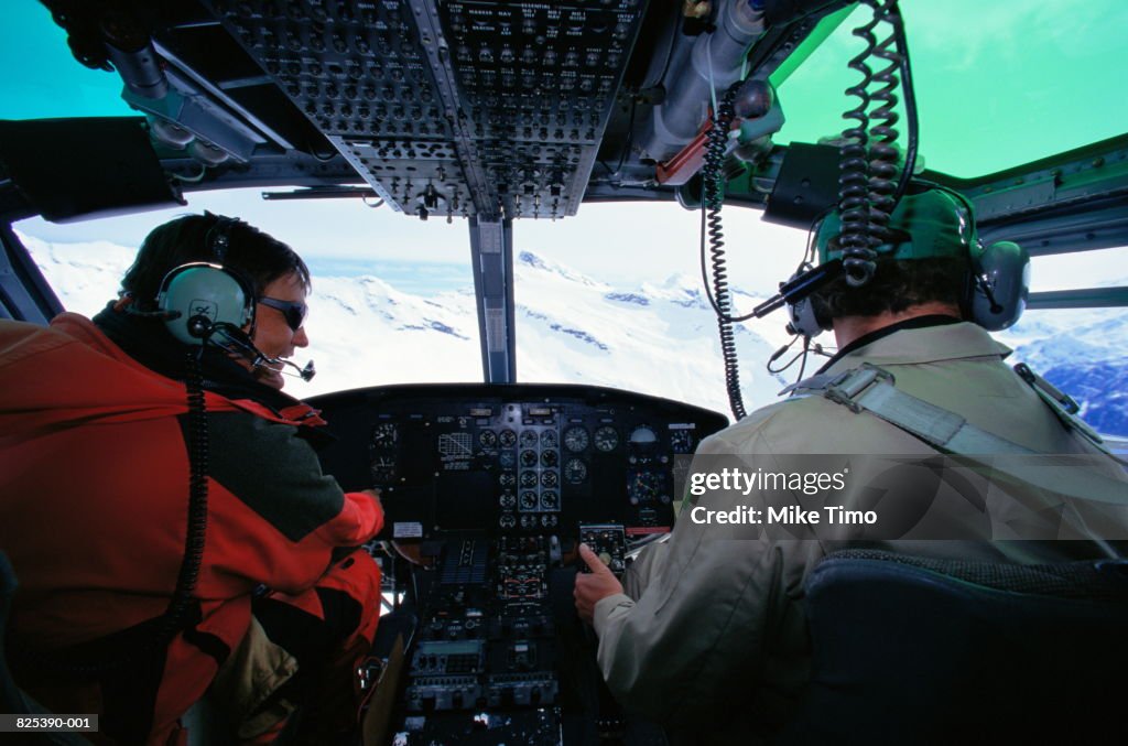 Pilot and passenger in helicopter cockpit, flying over mountains