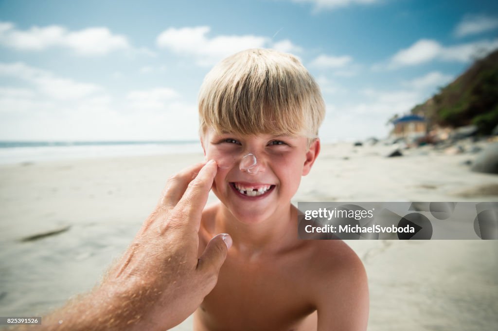 Dad Applying Sun Screen On His Boy At The Beach