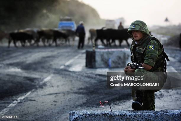 Russian peacekeeper looks on during the final moments of the forces' pull out on August 22, 2008 while a herd of cows passes behind him, in...