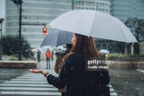 young woman with umbrella enjoying the snowfall in city street - catching snow stock pictures, royalty-free photos & images