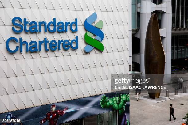 Pedestrians walk past Standard Chartered signage in the Central district of Hong Kong on August 2, 2017. - Standard Chartered's half-year results...