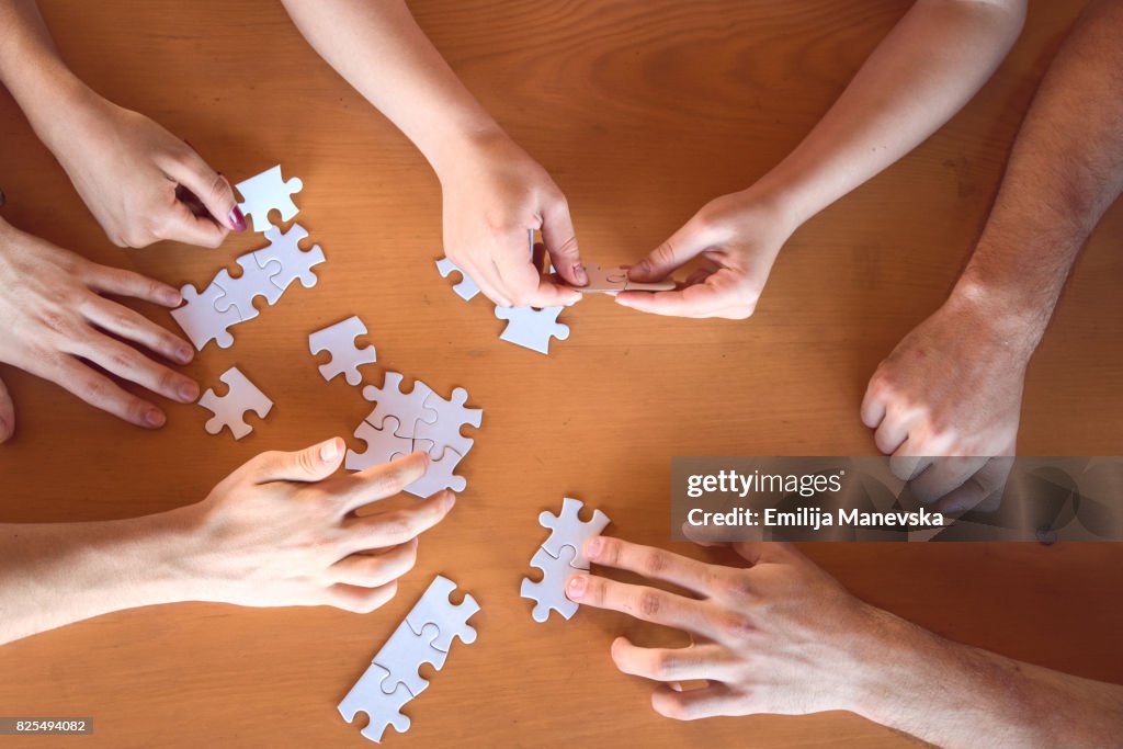 Young people sitting at desk, putting puzzle pieces together, finding solution