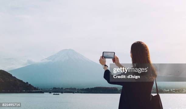 asian female tourist taking pictures of mt fuji with smartphone - capturar una imagen fotografías e imágenes de stock