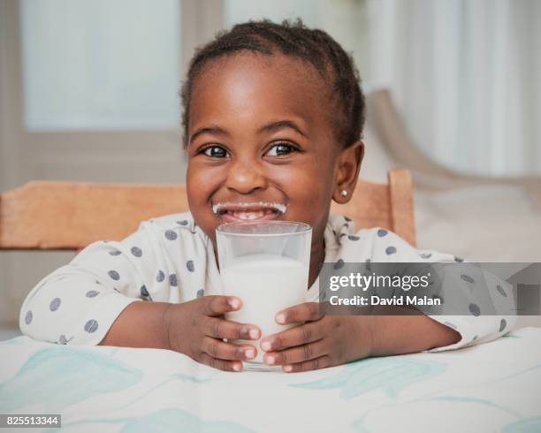 young african girl smiling (with a milk mustache) over a glass of milk. - milchbart stock-fotos und bilder