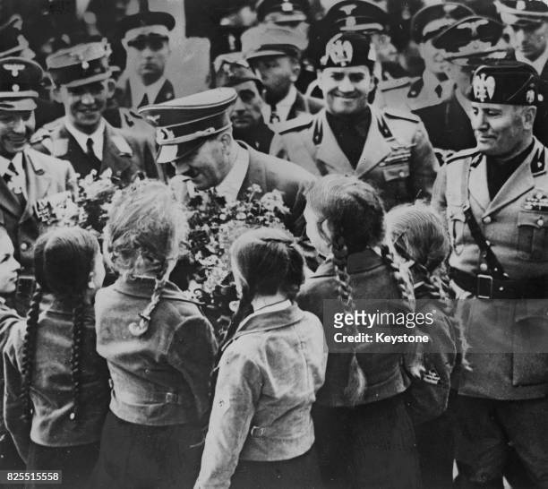 German Chancellor Adolf Hitler receives a bouquet from a group of girls upon his arrival at the old Roman Forum in Rome, Italy, with Italian Prime...