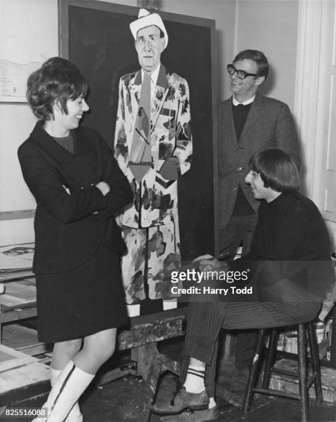 English comedian Roy Hudd and his wife Ann watch artist Barry Fantoni finish off his portrait of the late comedian Max Miller, 29th November 1966....