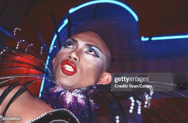 Transvestite with a shaved head and wearing heavy make-up strikes a dramatic pose as he competes in a beauty contest in a nightclub in downtown...