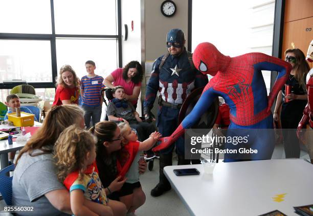 Costumed Spiderman reaches out to shake hands with one and a half year-old Maggie Mendonca, center, as her sister Leona left, looks on as Boston...