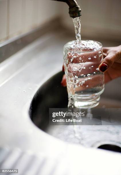 woman with glass of overflowing water under faucet - overflowing glass stock-fotos und bilder