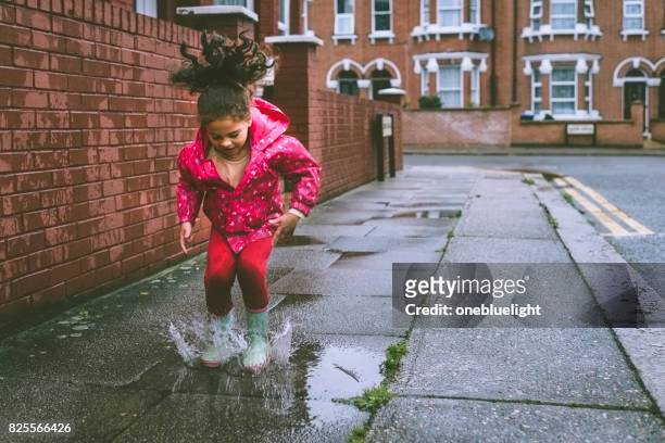 bambino (5-6) con stivali blu che saltano nelle pozzanghere. - puddle foto e immagini stock