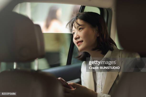 business woman who has a smartphone and is looking out the window of the car - south korea woman stock pictures, royalty-free photos & images