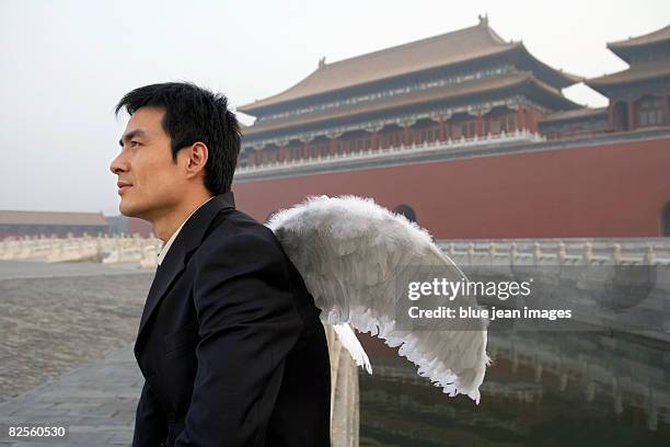 a man in business attire with wings, looks into the distance, chinese architectural elements behind. - anjo da guarda imagens e fotografias de stock