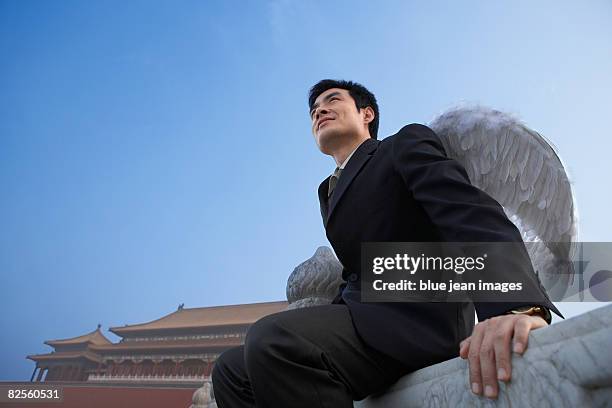 a man in business attire with wings, looks into the distance, chinese architectural elements behind. - anjo da guarda imagens e fotografias de stock