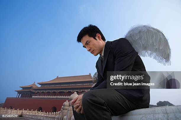 a man in business attire with wings, looking introspective, chinese architectural elements behind. - anjo da guarda imagens e fotografias de stock