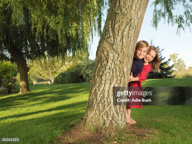 young boy and girl hiding behind tree - hiding behind bush stock pictures, royalty-free photos & images