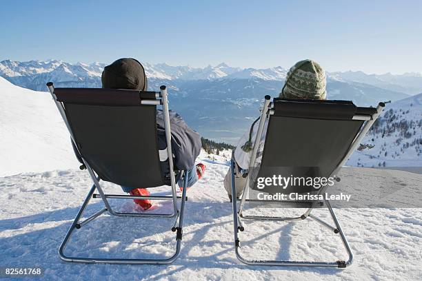 man, woman relax on deck chairs in snow - zurücklehnen stock-fotos und bilder