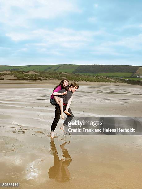 man carrying woman piggy back on beach - croyde beach stock pictures, royalty-free photos & images