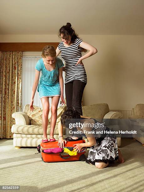 three females trying to close suitcase. - suitcase close stock-fotos und bilder