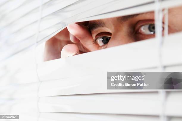 man looking through office blinds - gluren stockfoto's en -beelden
